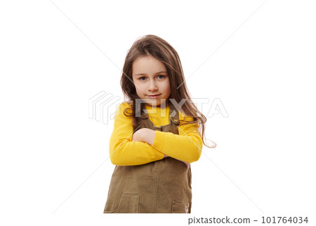 Portrait of a Caucasian smiling little schoolgirl in stylish casual dress, standing with her hands folded, smiling looking confidently at camera, isolated on white background. Schoolgirl. Education Portrait of a Caucasian smiling little schoolgirl in stylish casual dress, standing with her hands folded, smiling looking confidently at camera, isolated on white background. Schoolgirl. Education 101764034