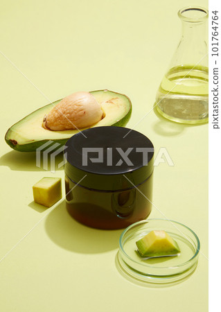 A glass petri dish with Avocado slice placed on, erlenmeyer flask containing essential oil extracted from Avocado (Persea americana) arranged with an empty label jar. Natural cosmetic concept 101764764