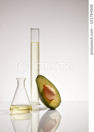 Front view of fresh half an avocado with seeds, test tube and erlenmeyer flask containing yellow liquid on white background. Concept laboratory and research natural extract making cosmetics 101764806
