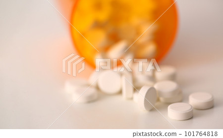 White pills are scattered near overturned jar on table White pills are scattered near overturned jar on table 101764818
