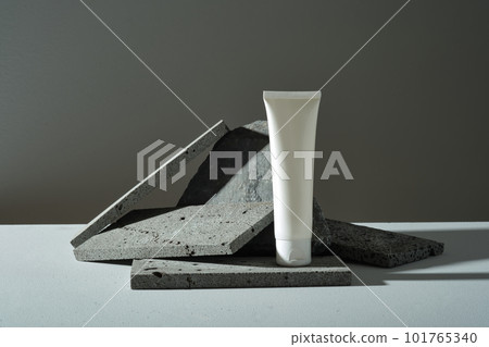 Dark rectangle stones are randomly decorated and white plastic bottle without label on black background. Minimal style, mockup for cosmetic, facial moisturizer cream or facial cleanser 101765340