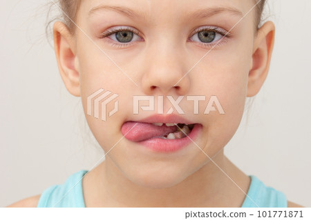 Child face with tongue out to left side cropped head caucasian little girl of 6 7 years on grey background Child face with tongue out to left side cropped head caucasian little girl of 6 7 years on grey background 101771871