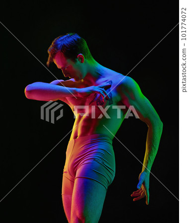 One young attractive man, dancer wearing nude clothes dancing with feelings over dark studio background with neon light. Emotional dance 101774072