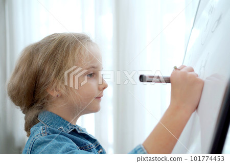 Lovely little cute girl enjoy drawing a picture and painting on a whiteboard. Elementary school age of little girl concentrate drawing on whiteboard or canvas. 101774453