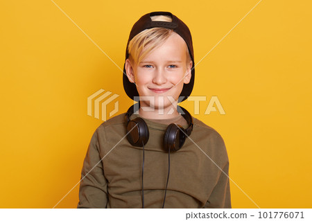 Horizontal studio picture of blond haired sweet kid having pleasant facial expression, smiling sincerely, having headphones around neck, being in good mood, spending time alone. Childhood concept. Horizontal studio picture of blond haired sweet kid having pleasant facial expression, smiling sincerely, having headphones around neck, being in good mood, spending time alone. Childhood concept. 101776071