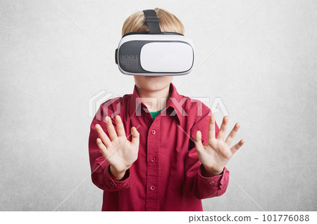 Augmented reality, children and entertainment concept. Small child in virtual headset enjoys beautiful and exciting pictures, stratches hands, imagines everything, gestures actively indoor 101776088