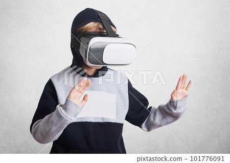 Photo of small kid wears virtual relality goggles, experiences something excited, gestures, entertains himself. Child in VR glasses with arms stretched forward and palms up, gropes something invisable Photo of small kid wears virtual relality goggles, experiences something excited, gestures, entertains himself. Child in VR glasses with arms stretched forward and palms up, gropes something invisable 101776091