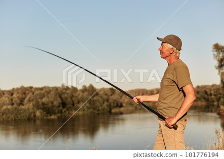 Fisherman using rod fly fishing in river, standing at bank of lake with concentrated look, catching fish, wearing casual clothing, spends time outdoors. 101776194