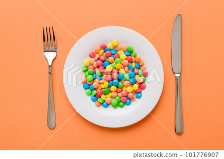 cutlery on table and sweet plate of candy. Health and obesity concept, top view on colored background cutlery on table and sweet plate of candy. Health and obesity concept, top view on colored background 101776907