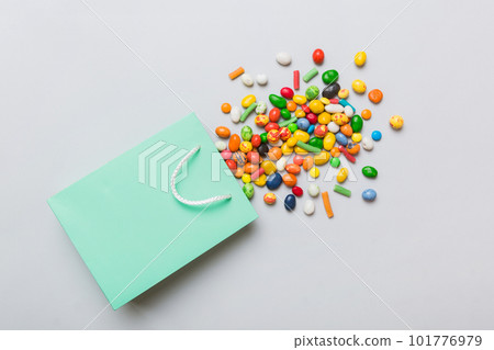 shopping paper gift bag in corner full of assorted traditional candies falling out on colored background with copy space. Happy Holidays sale concept 101776979