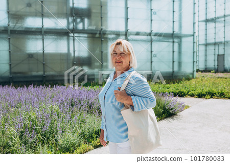 Mature blonde woman in casual summer clothes holding white canvas tote bag. Mockup and zero waste concept. Eco Nature Friendly Style. Environmental Conservation Recycling mock up 101780083