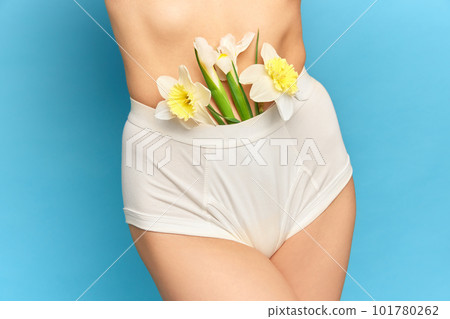 Close up portrait with sensual, young female body wearing white underwear and holding flower in hand on bright studio background. Diet for flat stomach Close up portrait with sensual, young female body wearing white underwear and holding flower in hand on bright studio background. Diet for flat stomach 101780262