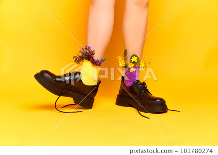 Funny female close up portrait with feet wearing classic shoes and wildflowers inside yellow studio background. Spring weather 101780274