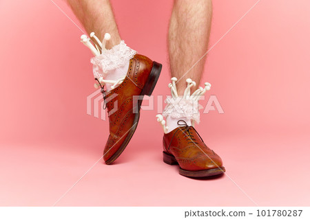 Close up portrait of male feet wearing shoes and white fancy socks with mushrooms inside on pink studio background. New spring fashion Close up portrait of male feet wearing shoes and white fancy socks with mushrooms inside on pink studio background. New spring fashion 101780287