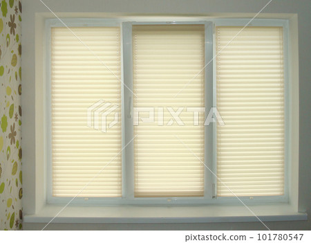 Pleated blinds close-up on the window in the interior. Home blinds - cordless pleated modern shades on apartment windows. Bottom up top down pleated curtains. Beige color fabric. Closed. Pleated blinds close-up on the window in the interior. Home blinds - cordless pleated modern shades on apartment windows. Bottom up top down pleated curtains. Beige color fabric. Closed. 101780547