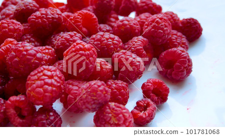 Red berries of ripe juicy large raspberries are scattered on a white table. Vitamin dessert 101781068