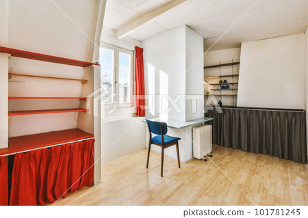 a small room with a desk and some shelves on the wall behind it is a window that looks out onto the street 101781245