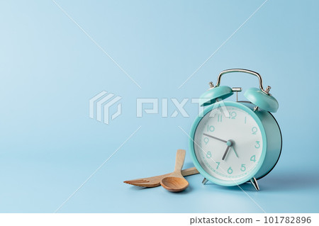 An alarm clock with cutlery set against blue background 101782896