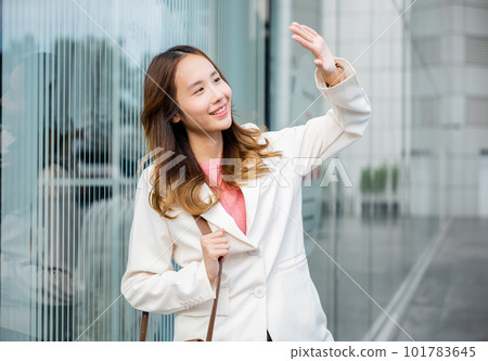 Happy woman wearing white suit jacket with brown bag at sunlight outdoors. Portrait of confidence young businesswoman standing outside office building in city raise your hand to shade sun Happy woman wearing white suit jacket with brown bag at sunlight outdoors. Portrait of confidence young businesswoman standing outside office building in city raise your hand to shade sun 101783645