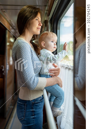 Family traveling in a train and looking through window. Mom shows his baby something outside window. Woman with child traveling by public transport. Family traveling in a train and looking through window. Mom shows his baby something outside window. Woman with child traveling by public transport. 101784245