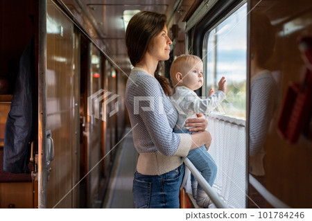 Family traveling in a train and looking through window. Mom shows his baby something outside window. Woman with child traveling by public transport. 101784246