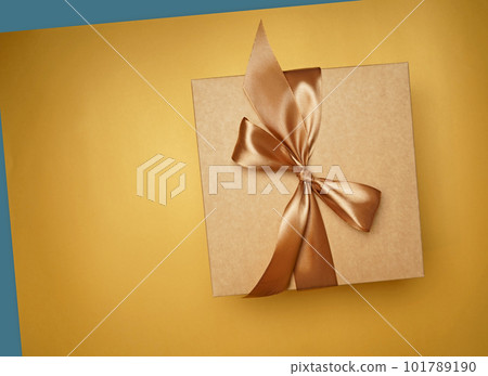 Surprise, gift. top view of small gift box tied with golden ribbon on yellow background 101789190