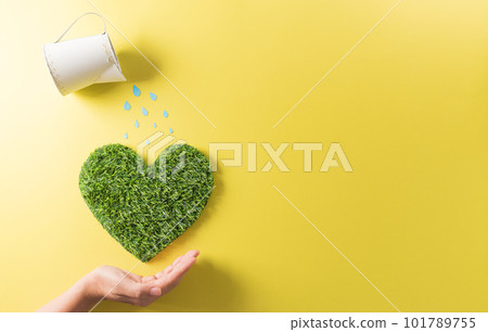 Hands holding green heart with watering on yellow background. World environment day, earth day, save earth and eco concept. 101789755