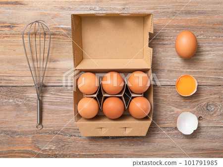 Tray with organic brown eggs with yolk,whisk and shell on white wooden table 101791985