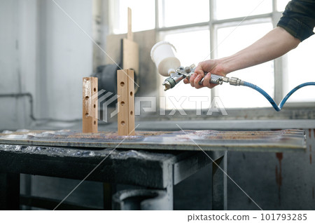 Young man carpenter wearing protective clothes varnishing board at workshop 101793285