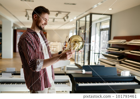 Handsome stylish male customer holding trumpet in hand standing at music shop 101793461