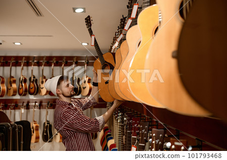 Young male owner of musical instrument shop putting guitar at display case 101793468