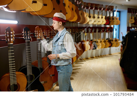 Young hipster woman buyer choosing acoustic guitar in instrument shop 101793484