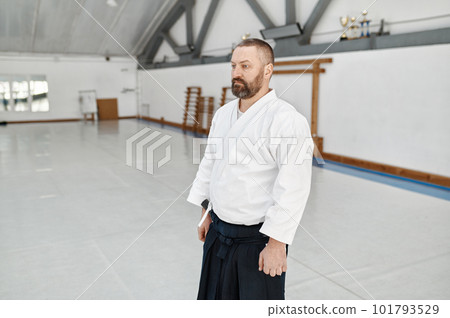 Serious aikido coach wearing kimono posing over empty sport gym background 101793529