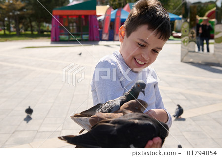 Friendly joyful pre teen boy, adorable child feeds pigeons in city summer park. The concept of kindness and care for animals. Childhood. Children. People. Nature 101794054