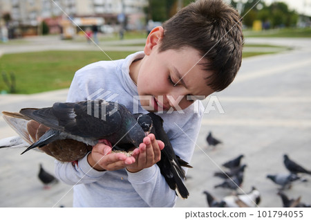 Close-up portrait of a schoolboy feeding rock pigeons in the park. The concept of kindness, walking with benefits, love and care for animals. Installing compassion for animals from childhood 101794055