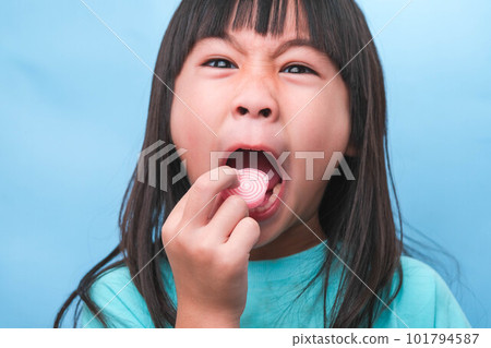 Smiling cute little girl eating sweet gelatin with sugar added isolated on blue background. Children eat sugary sweets, causing loss teeth or tooth decay and unhealthy oral care. Smiling cute little girl eating sweet gelatin with sugar added isolated on blue background. Children eat sugary sweets, causing loss teeth or tooth decay and unhealthy oral care. 101794587