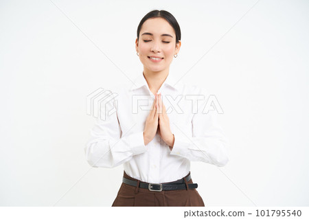 Smiling calm young woman, holds hands in pray with eyes closed, makes wish, hopes for smth, white background 101795540