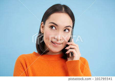 Cheerful asian girl talks on mobile phone, speaks with someone on telephone, stands over blue background 101795541