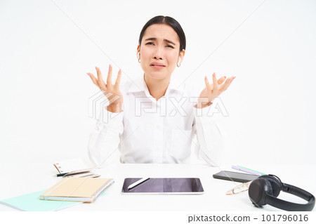 Business and corporate people. Asian office employee sits in workplace, complains, shakes hands with frustrated face, white background Business and corporate people. Asian office employee sits in workplace, complains, shakes hands with frustrated face, white background 101796016