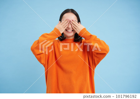 Portrait of cheerful cute asian girl waits for surprise, shuts her eyes with hands, birthday girl awaiting for gift, stands over blue background 101796192