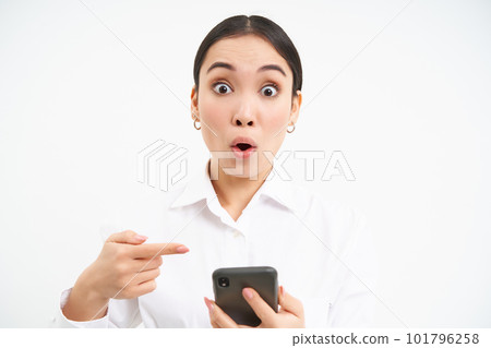 Close up portrait of happy saleswoman, successful woman with smartphone, pointing at her phone and smiling amazed, standing over white background Close up portrait of happy saleswoman, successful woman with smartphone, pointing at her phone and smiling amazed, standing over white background 101796258