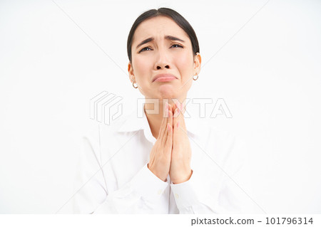 Upset asian woman looks up with desperate and sad face, complains to Lord, stands over white background Upset asian woman looks up with desperate and sad face, complains to Lord, stands over white background 101796314