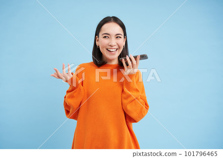 Happy asian woman records voice message, repeats words in language learning mobile app, talks in smartphone speakerphone, blue background 101796465