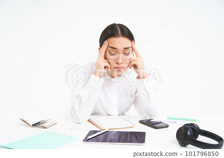 Workplace and business. Portrait of tired woman in office, company employee sits at desk with exhausted face, touches her head, has headache, white background Workplace and business. Portrait of tired woman in office, company employee sits at desk with exhausted face, touches her head, has headache, white background 101796850