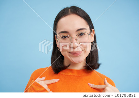 Portrait of beautiful girl in stylish glasses, pointing at herself with confidence, being self-assured, standing over blue background 101796851