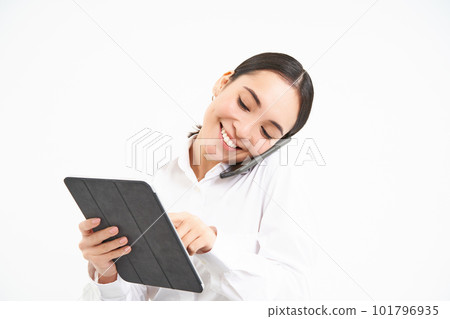 Asian working businesswoman discussing business over the phone, talking on cellphone and looking at digital tablet, standing over white background 101796935