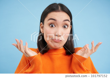 Close up of surprised japanese woman, shrugs and spreads hands sideways, looks confused, stands over blue background Close up of surprised japanese woman, shrugs and spreads hands sideways, looks confused, stands over blue background 101797152
