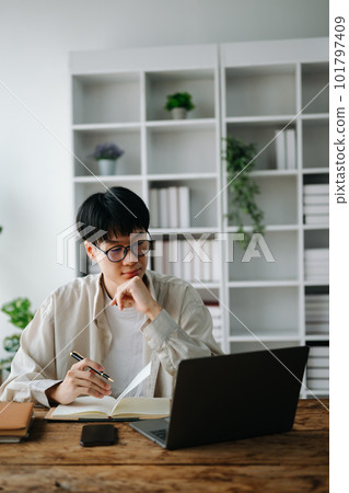 Male student taking notes from a book at library, Young asian sitting at desk doing assignments in college library Male student taking notes from a book at library, Young asian sitting at desk doing assignments in college library 101797409