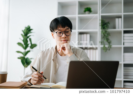 Male student taking notes from a book at library, Young asian sitting at desk doing assignments in college library Male student taking notes from a book at library, Young asian sitting at desk doing assignments in college library 101797410