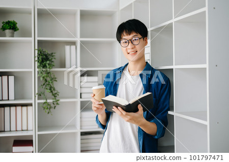 Male student taking notes from a book at library, Young asian sitting at desk doing assignments in college library 101797471